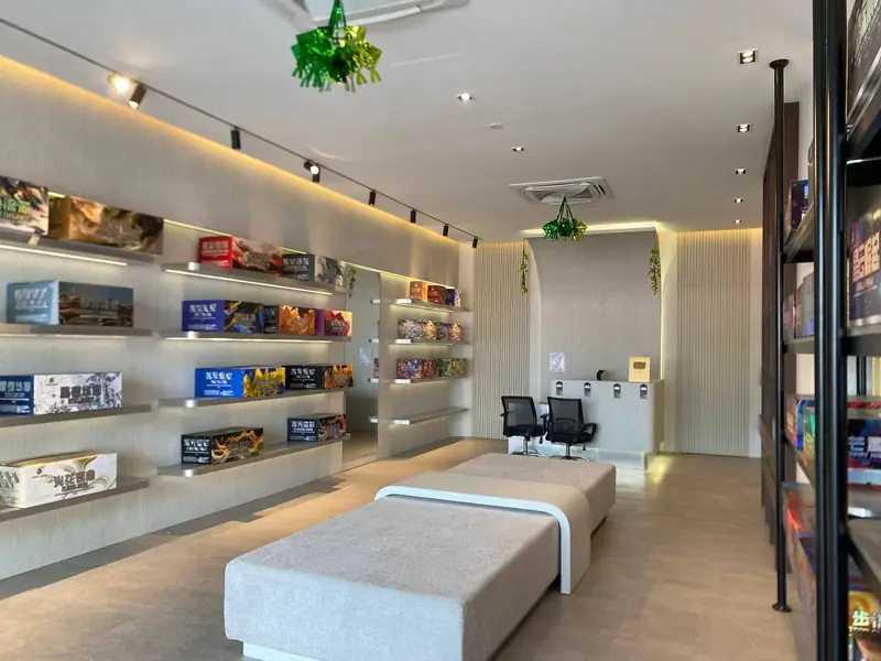 The Bangi showroom: a long lit shelf wall of printed cartons on one side, a bench down the middle and a working desk at the end.
