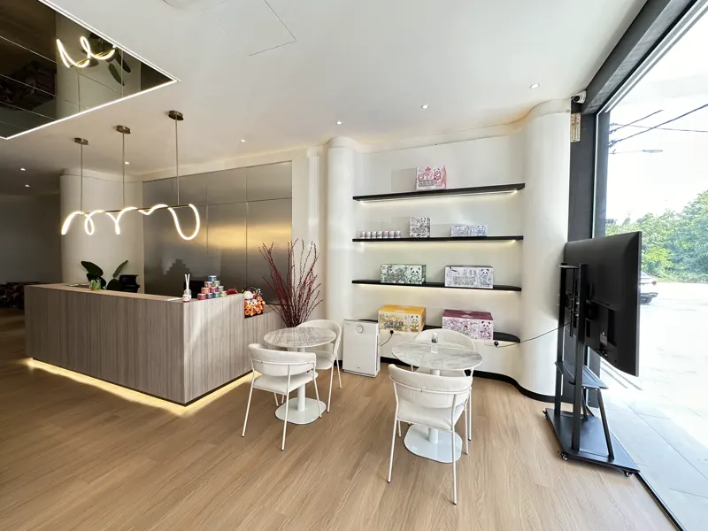 Just inside the door: a pale reception counter, white tulip chairs and looping neon pendants beside floor-to-ceiling glass.