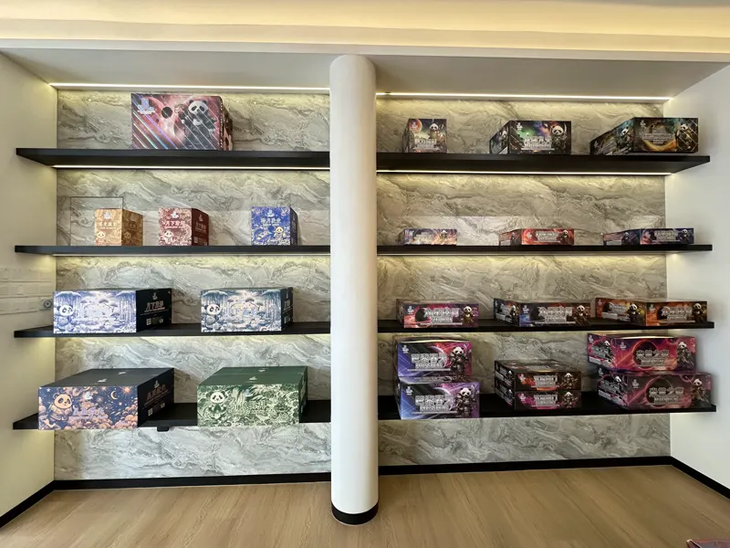 Black floating shelves lit strip by strip against a marble feature wall, each shelf holding boxed cake fireworks.