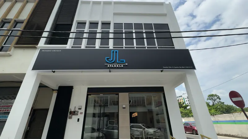 The JL Sparkle building on Jalan Syarikat 1 seen from the road: a dark signboard over full-height glass doors, with parking in front.